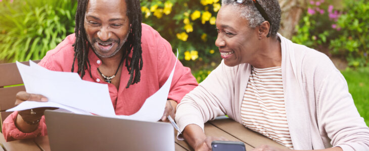 man and woman sitting at a table outside with documents and a computer