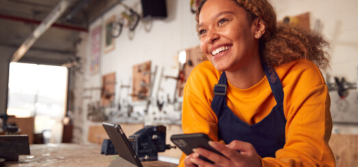 Female small business owner in orange sweater and black apron leaning over counter