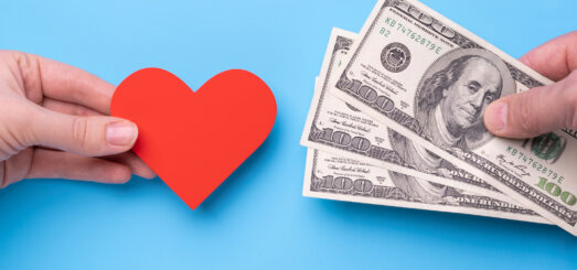 Male hand gives 300 dollars to female hand with red heart, blue background