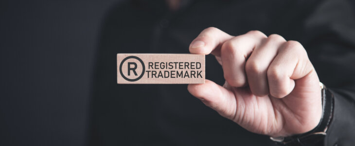 Male hand showing R-Registered trademark on wooden block.