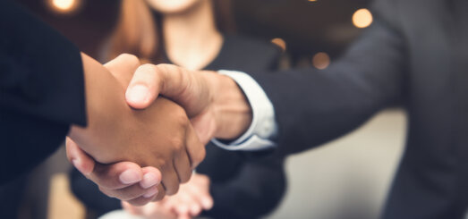 Businessmen shaking hands with businesswoman in background