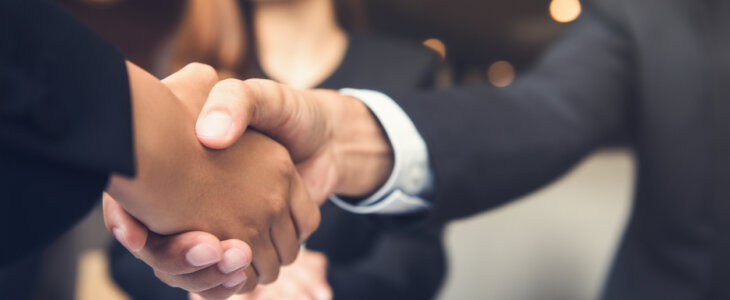 Businessmen shaking hands with businesswoman in background